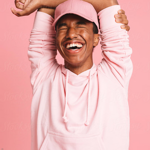 young man in pink hat and sweatshirt smiling with arms over head